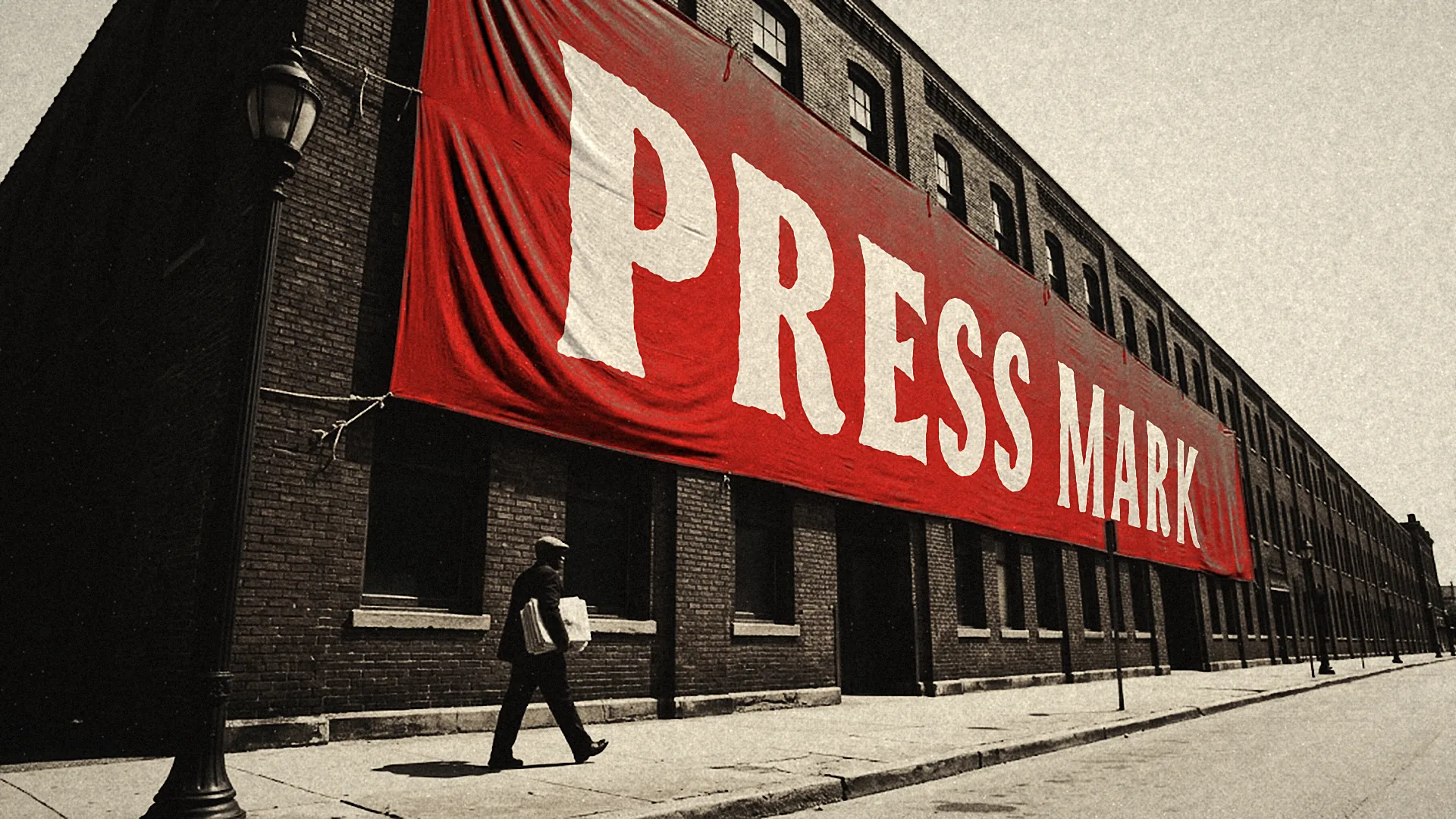 A giant red banner reading PRESS MARK runs along the wall of a long brick building as a lone man carries a parcel down the sidewalk.