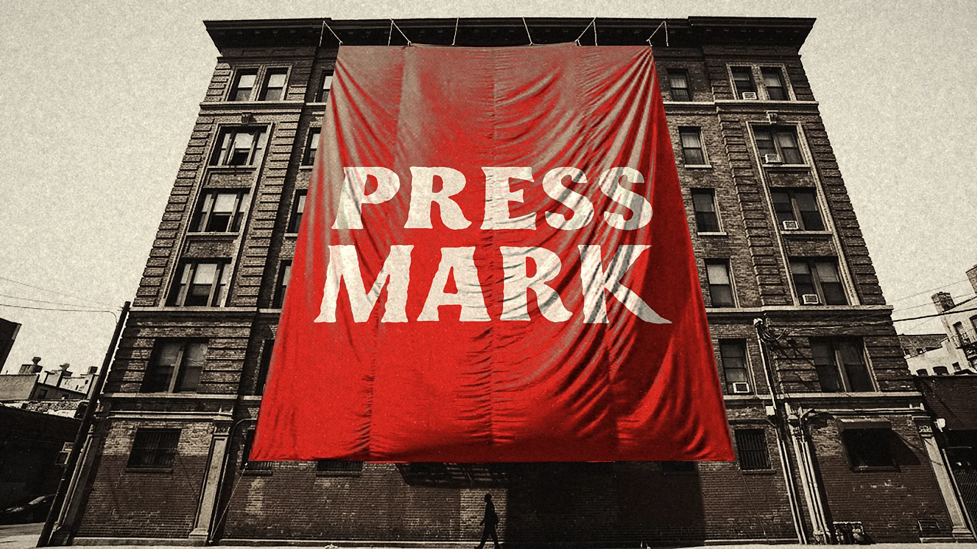 A giant red banner reading PRESS MARK hangs down the face of a tall brick building, seen from street level looking up.