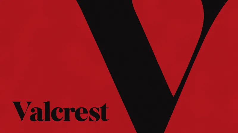 A giant black capital V of VALCREST, cropped by the top and bottom of the frame, on red, with the name Valcrest in black at the lower left.