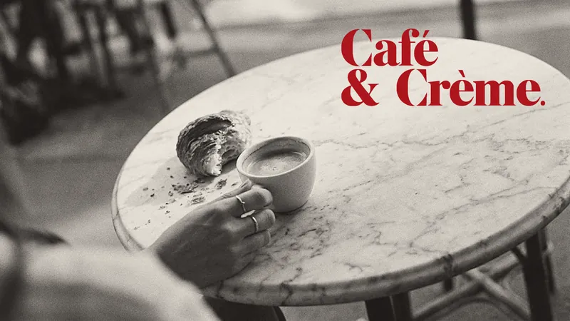 A black-and-white photograph of a café crème and a half-eaten croissant on a marble bistro table with the words Café & Crème. in red.
