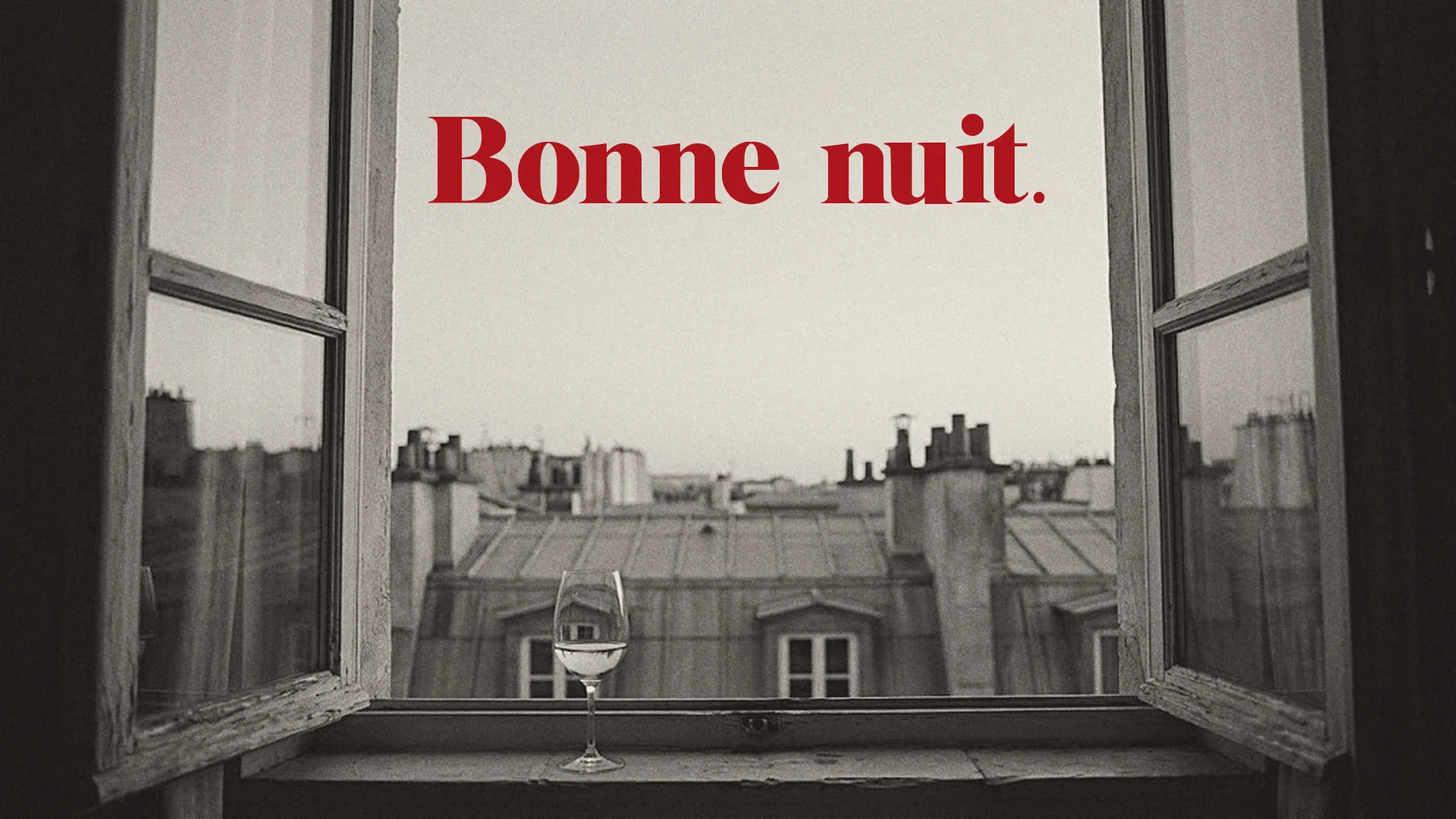 A black-and-white photograph of Paris rooftops through an open window with a glass on the sill and the words Bonne nuit. in red in the sky.